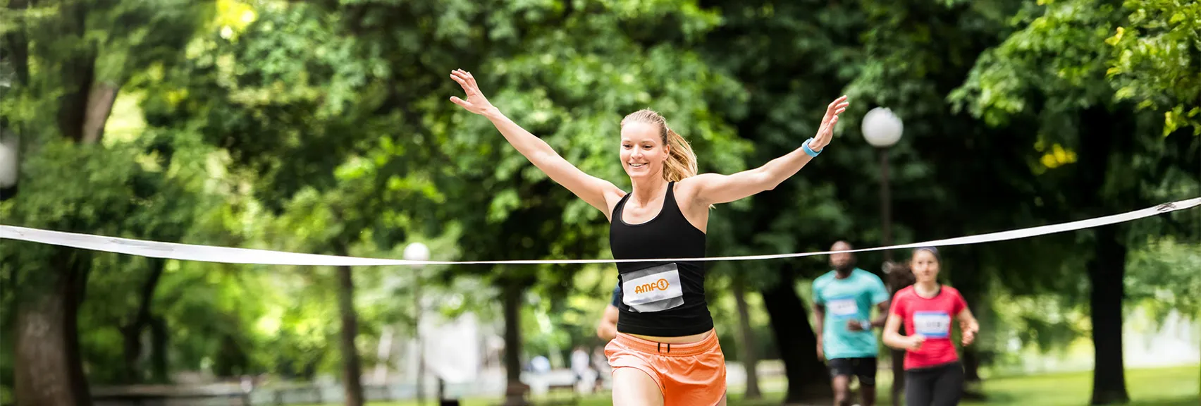 Profitieren Sie vom AMF Gesundheitskreis: Sport, Ernährung und Gesundheitsvorträge AMF Läuferin läuft durch ein Zielband – Symbolbild für den AMF Gesundheitskreis mit sportlichen Angeboten, gesundem Essen und Vorträgen
