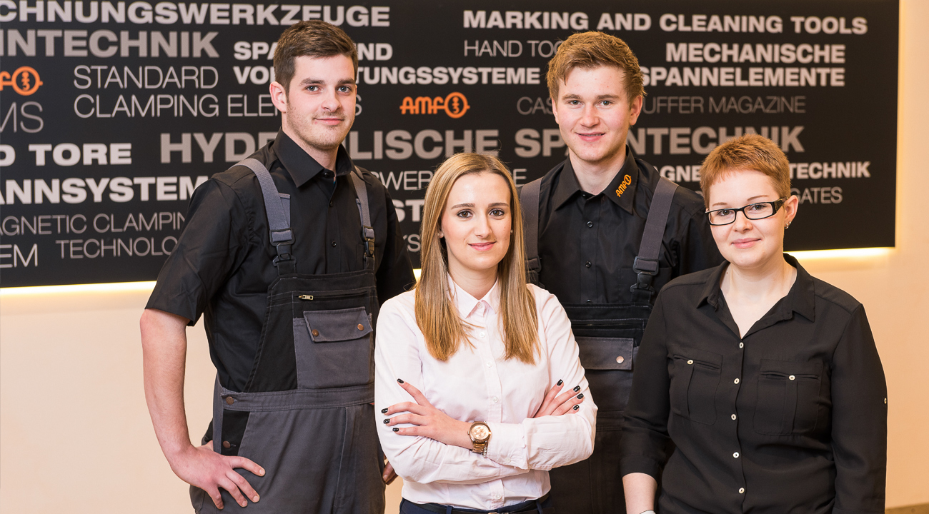 Vier Auszubildende bei AMF zeigen ihre Berufsbilder durch typische Kleidung